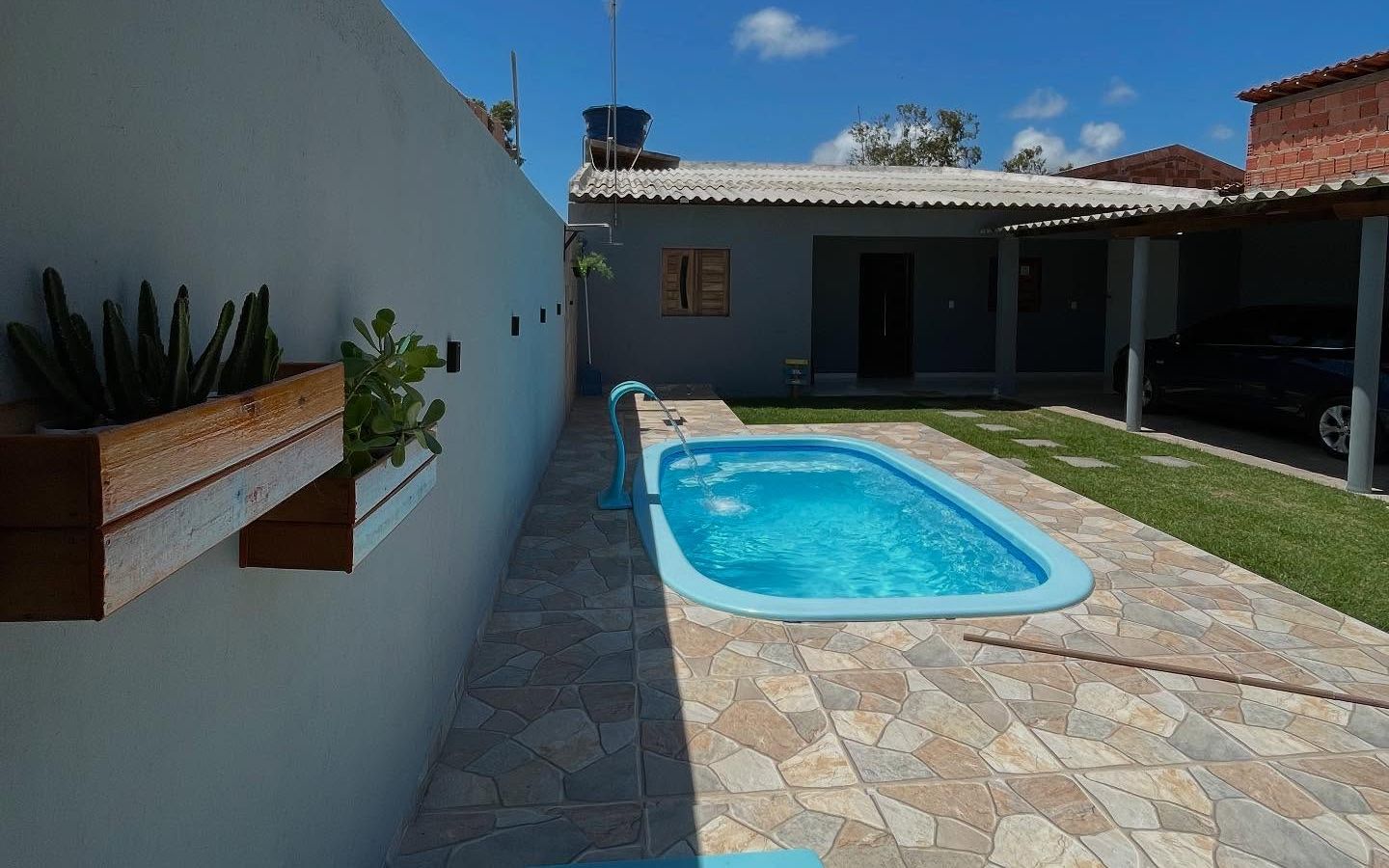 O quintal de dia: piscina, piso de pedra, gramado e a garagem coberta